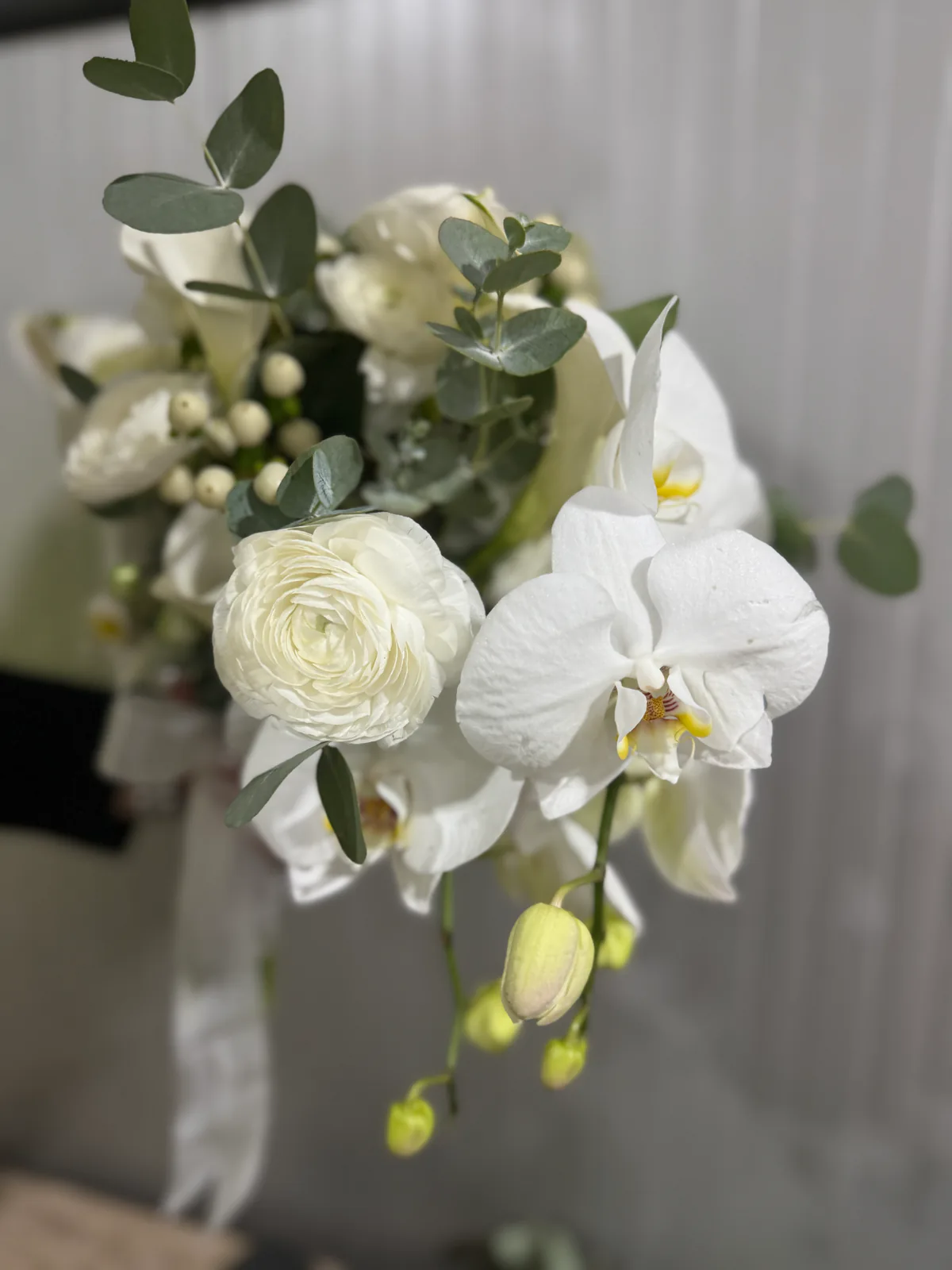 Detaliu de buchet de mireasă alb: ranunculus, orhidee și frunze de eucalipt