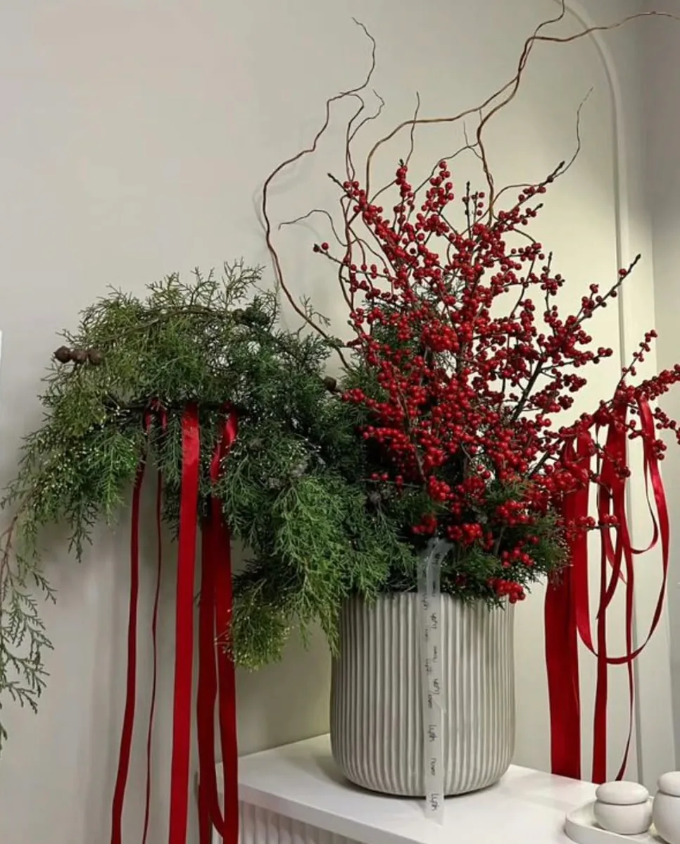 Aranjament de iarnă cu ilex roșu, cetină și panglici roșii, în vas de ceramică