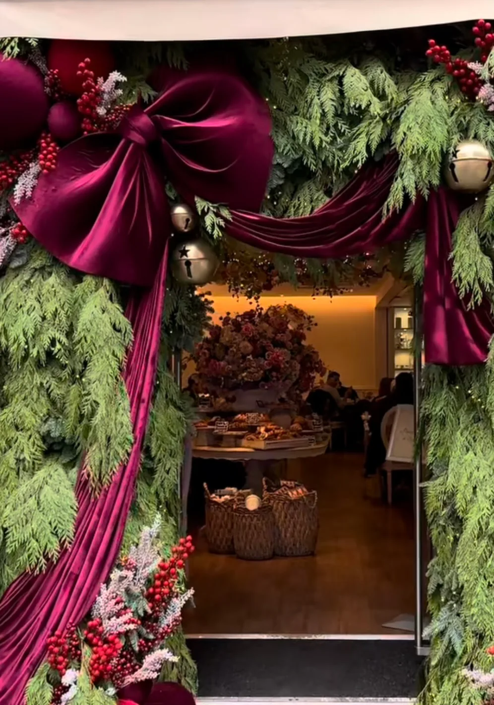 Intrarea unui restaurant decorată de Crăciun cu cetină, fundă mare din catifea bordo și globuri