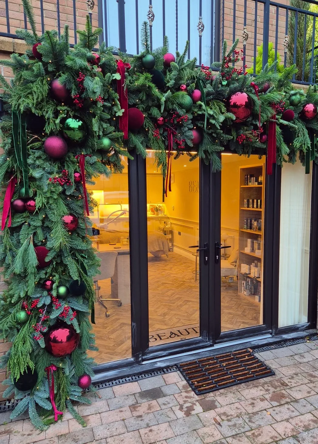 Vitrina unui salon decorată de Crăciun cu ghirlandă de brad și globuri verzi și bordo