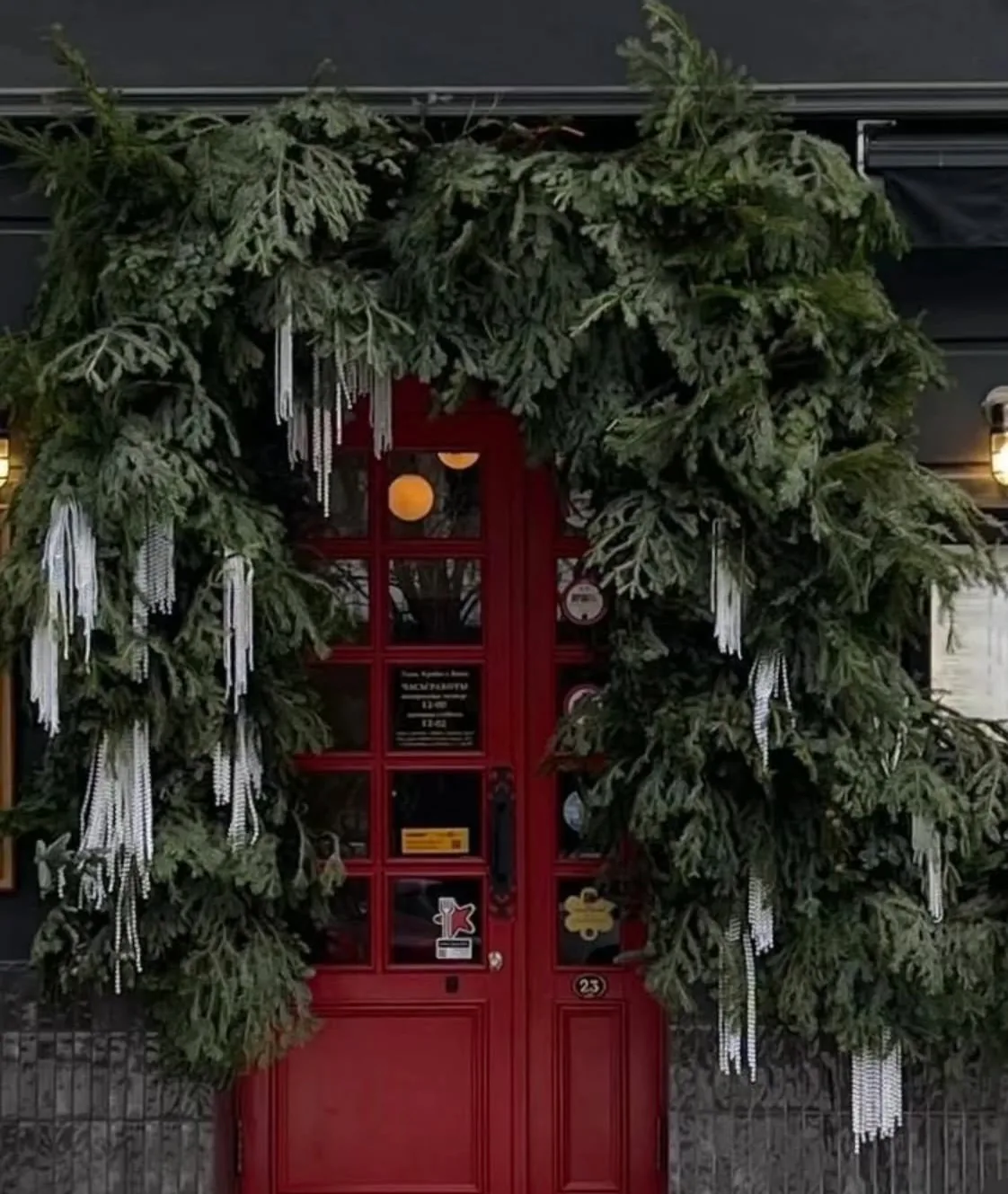 Ghirlandă de Crăciun peste ușa roșie a unui restaurant, cu cetină și țurțuri albi