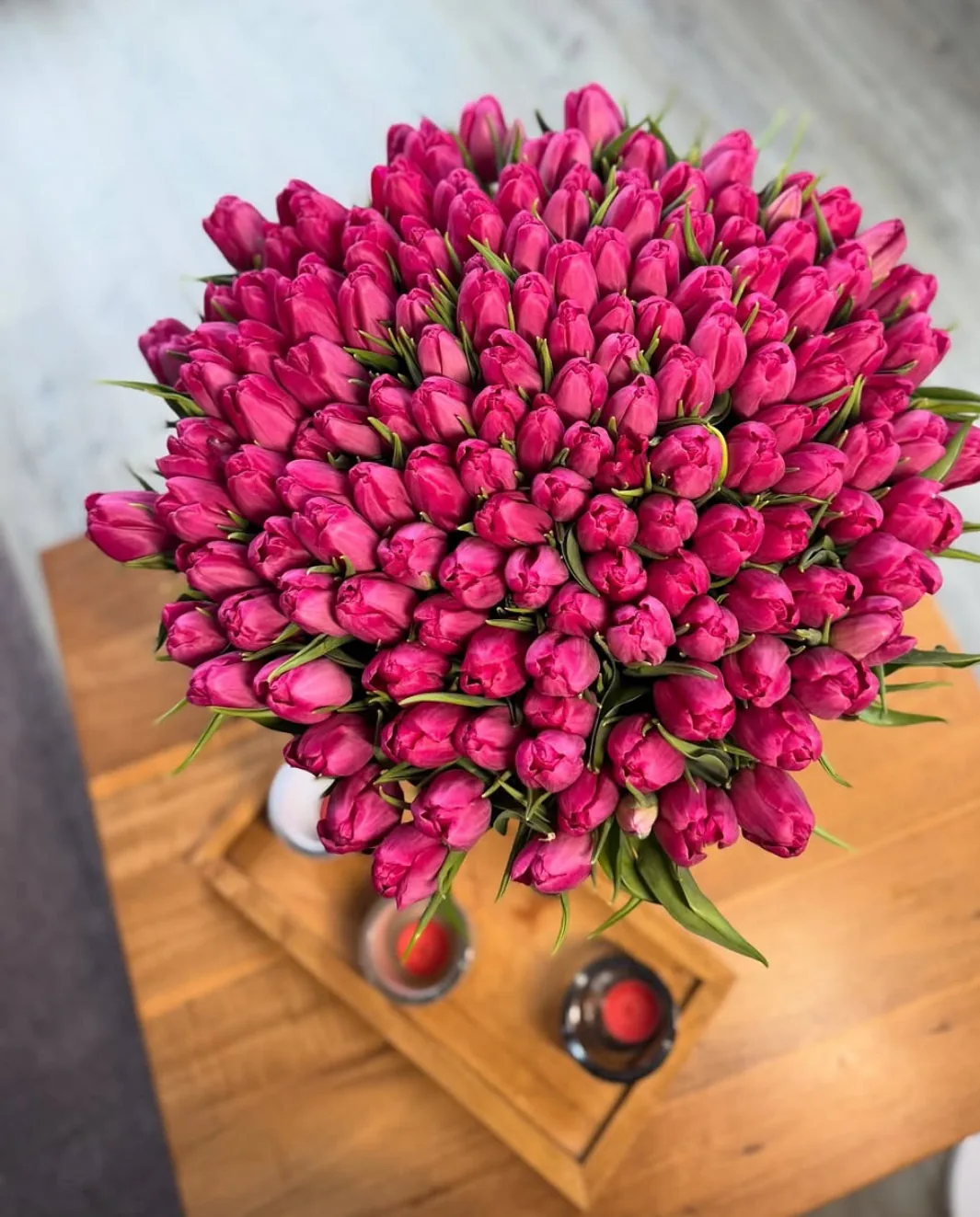 Buchet generos de lalele ciclam, așezat în vas pe o masă de lemn