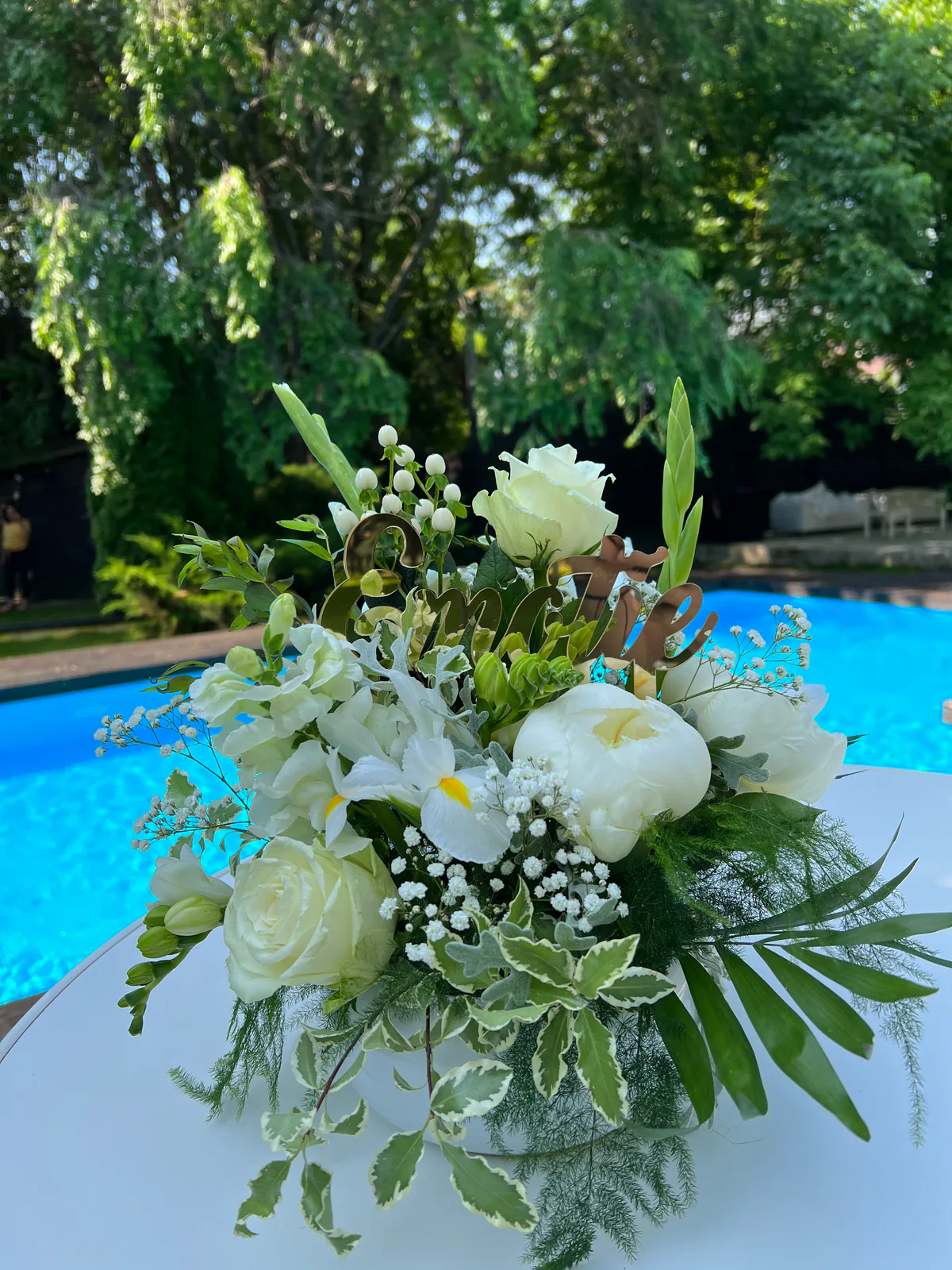 Aranjament floral alb cu trandafiri și verdeață, pe masa unui eveniment lângă piscină
