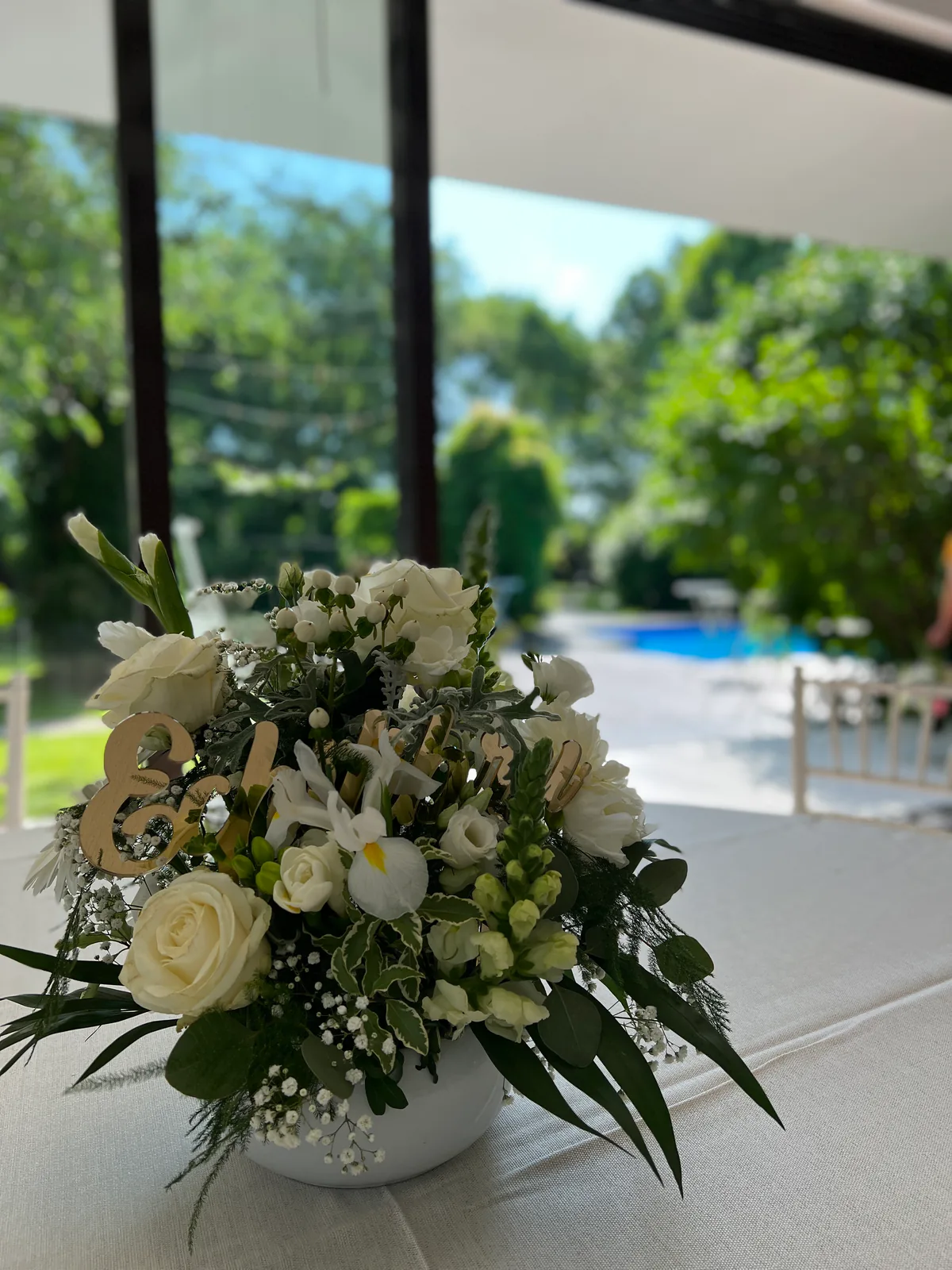 Aranjament floral alb-verde în vas ceramic, pe masa unui eveniment de vară în grădină